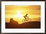 A woman rides her bike in the sunset with rock cliffs in the background Photography Framed Art Poster Print by Dugald Bremner, 29x21 A woman rides her bike in the sunset with rock cliffs in the background Photography Framed Art Poster Print by Dugald Bremner, 29x21