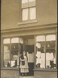Woman Standing in the Doorway of a Modest Clothing Shop Photographic Poster Print, 18x24
