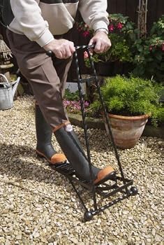 Black Boot Jack being used by person. Person is holding onto handles of metal boot jack removing Wellington boot.