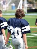 Young Football Player Carrying Helmet on Sideline - 24