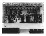 Historic Print (L): [14 women and 2 boys on a stage bordered with advertising plaques of business enterprise